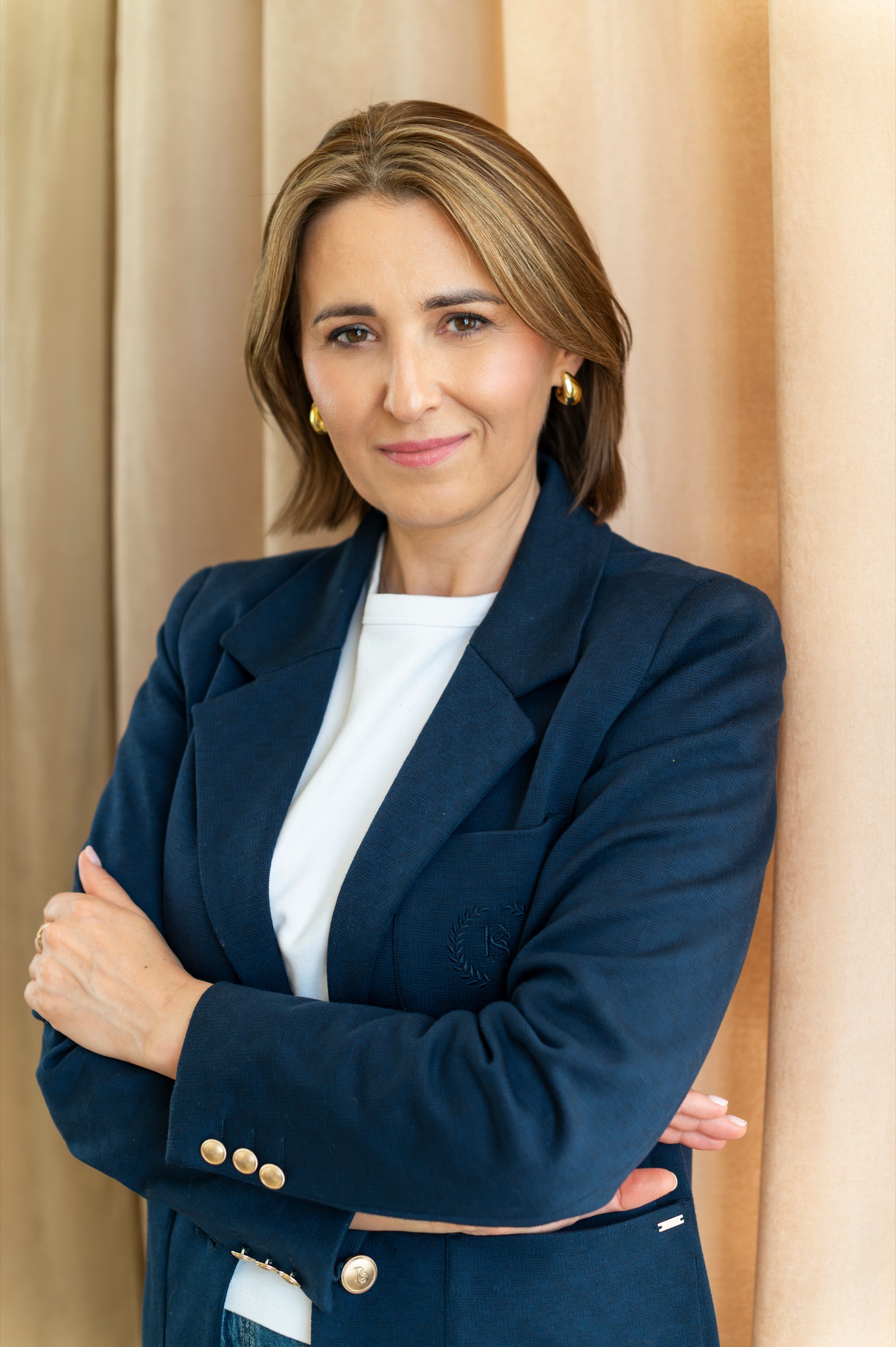 Portret Doroty Bazan do pasa, w granatowej marynarce, na tle beżowej zasłony