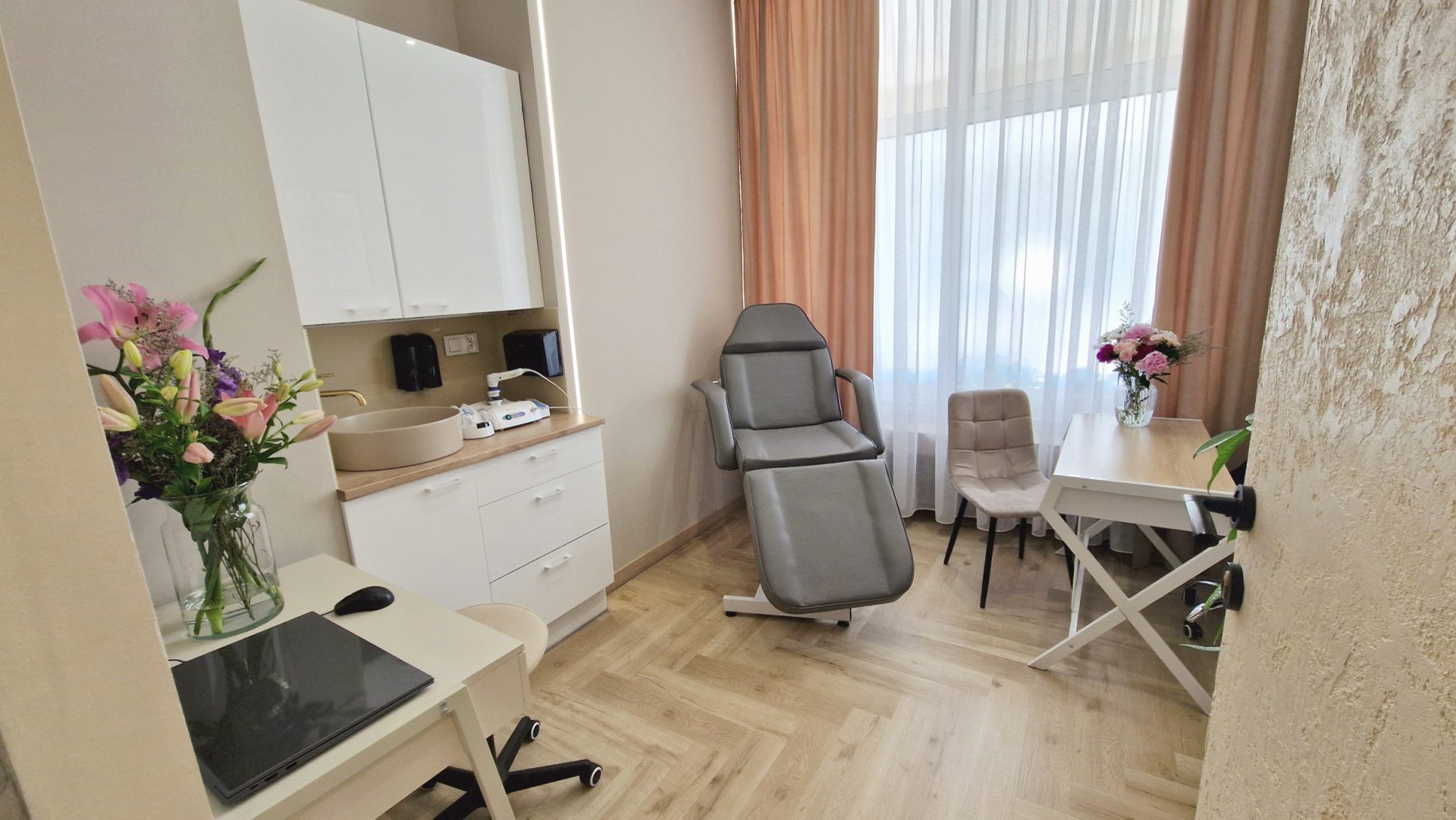 Gabinet zabiegowy nr 1 z szarym fotelem kosmetycznym, umywalką i stolikiem przy oknie